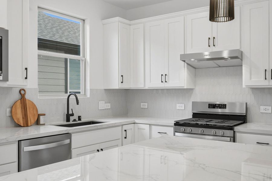 Natural light pours into this sleek kitchen, highlighting the marble countertops, stylish backsplash, and modern finishes throughout.