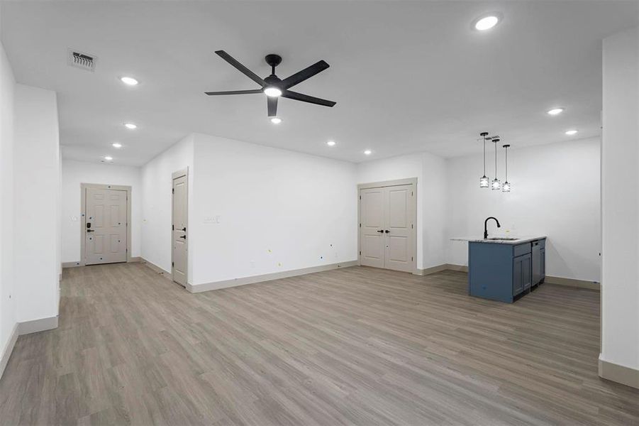 Unfurnished living room featuring a ceiling fan, visible vents, light wood finished floors, recessed lighting, and a sink