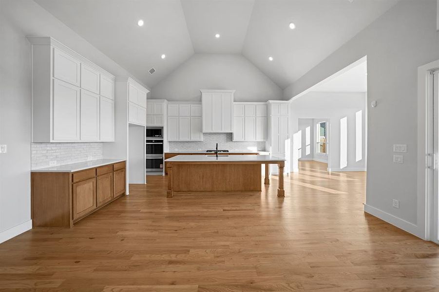 Kitchen featuring white cabinetry, tasteful backsplash, brown cabinetry, light wood-style floors, and high vaulted ceiling Kitchen featuring white cabinetry, tasteful backsplash, brown cabinetry, light wood-style floors, and high vaulted ceiling