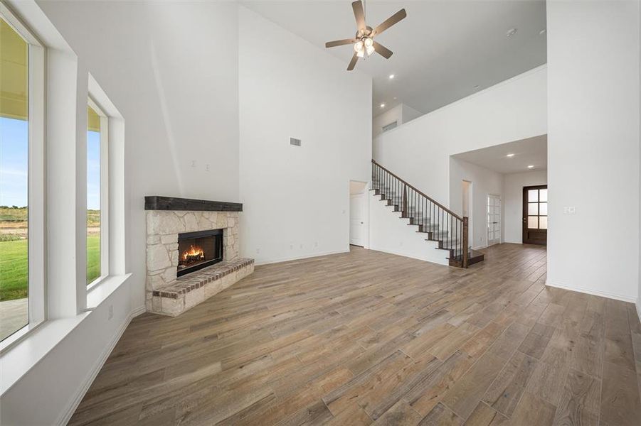 Unfurnished living room with wood finished floors, a towering ceiling, stairs, a fireplace, and a ceiling fan Unfurnished living room with wood finished floors, a towering ceiling, stairs, a fireplace, and a ceiling fan