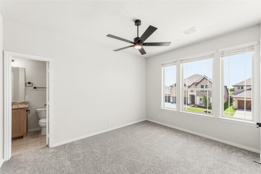 Bedroom with carpet, ceiling fan, three windows, and ensuite bathroom visible through open door