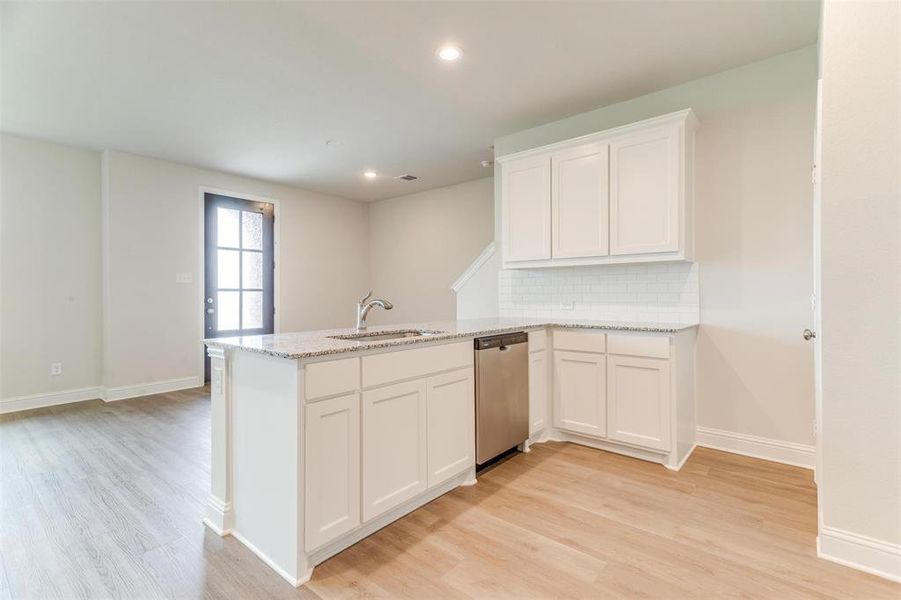 Kitchen featuring white cabinetry, sink, stainless steel dishwasher, and light stone countertops