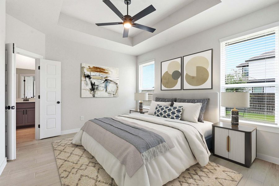 A comfortable bedroom features a tray ceiling, ceiling fan, and large windows with blinds.