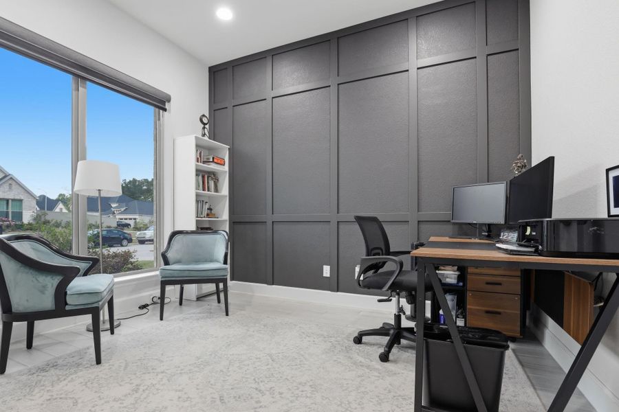 The dedicated study is anchored by a dark accent wall with grid molding and an oversized window overlooking the front.