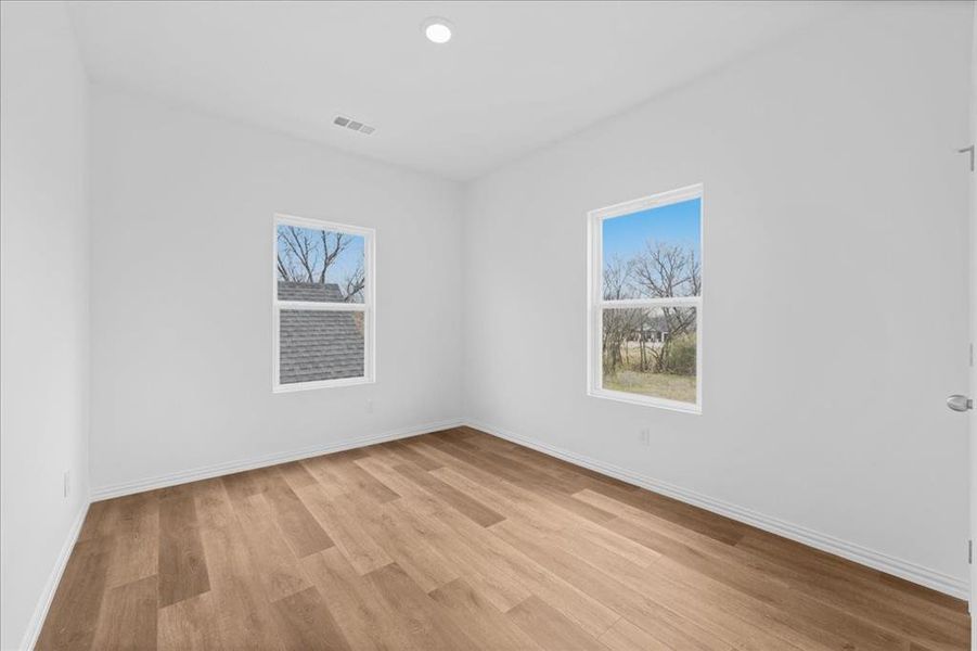 Bright secondary bedroom featuring wood-look flooring, neutral paint, and ample natural light. Comfortable layout with clean, modern finishes.