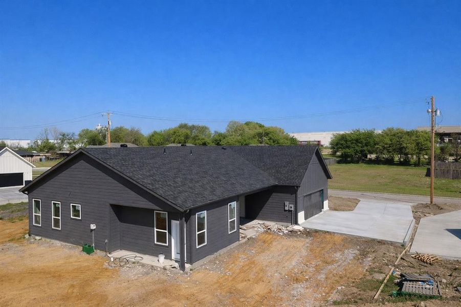 View of side of property featuring concrete driveway, a shingled roof, an attached garage, and a patio area