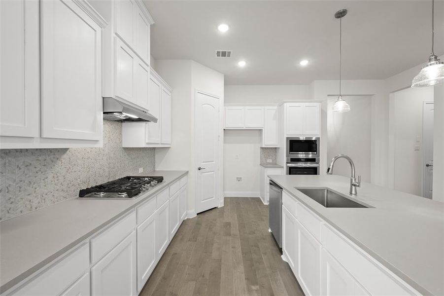 Kitchen with a sink, stainless steel appliances, wood finished floors, white cabinetry, and recessed lighting Kitchen with a sink, stainless steel appliances, wood finished floors, white cabinetry, and recessed lighting