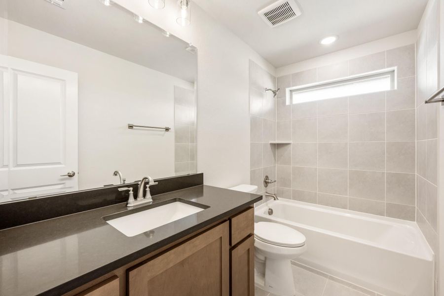 Bathroom with dark countertop vanity, tiled tub-shower combo, and white toilet Bathroom with dark countertop vanity, tiled tub-shower combo, and white toilet