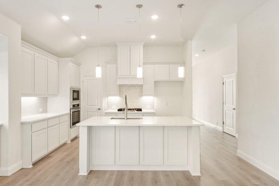 White kitchen with large center island, pendant lights, double ovens, and light hardwood floors