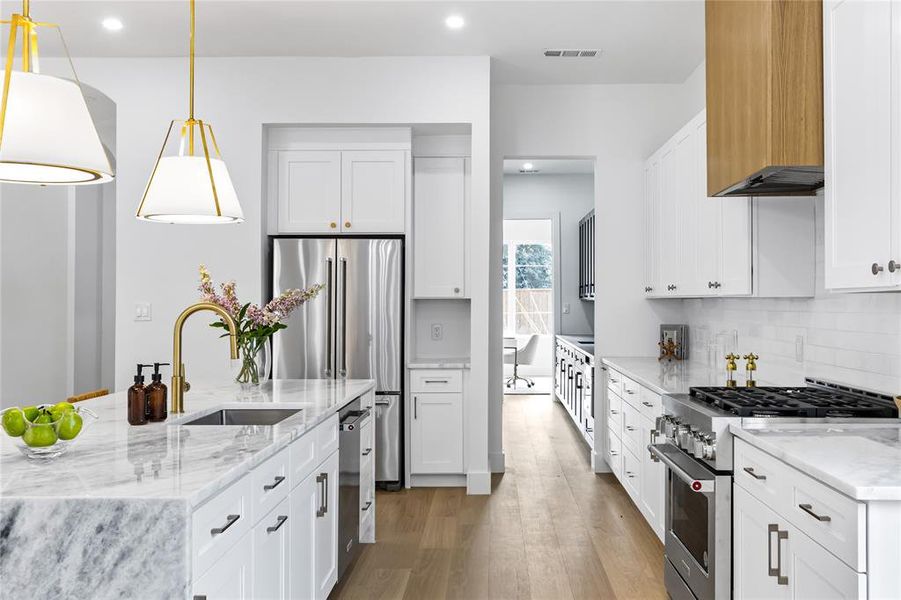 Kitchen with high end appliances, white cabinetry, and pendant lighting