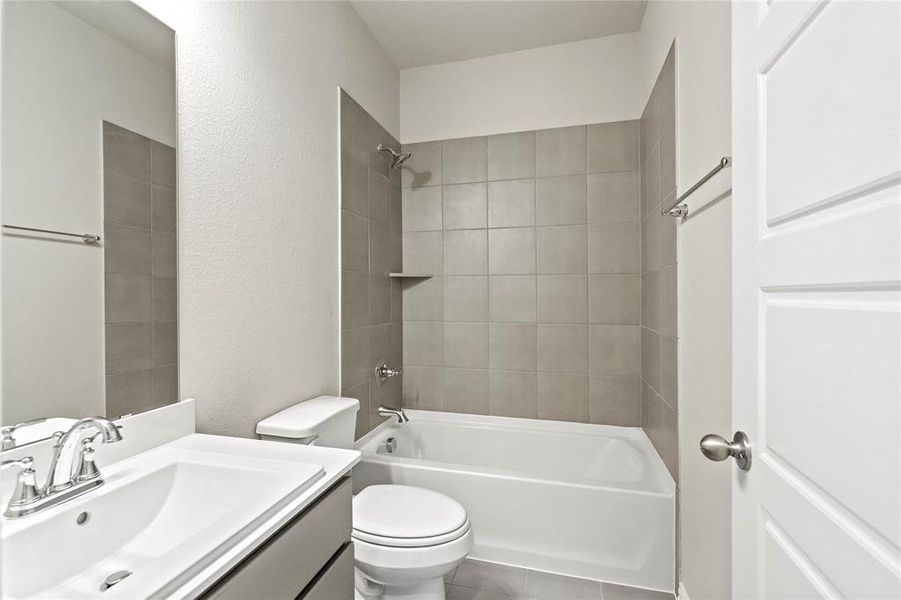 Full bathroom with tile patterned flooring, toilet, vanity, and tiled shower / bath