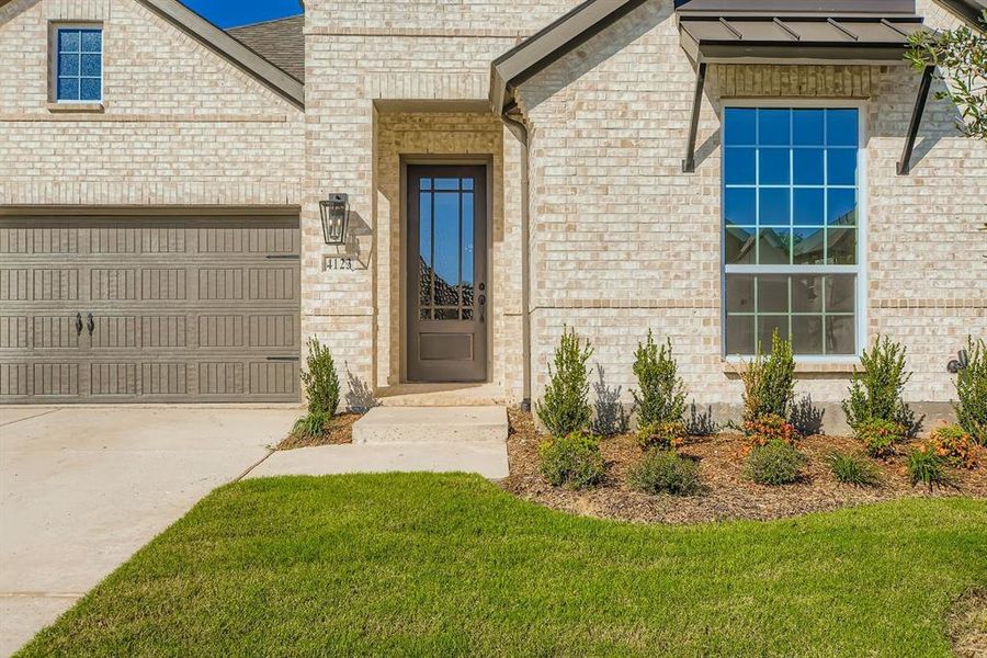 View of exterior entry featuring brick siding, driveway, an attached garage, and a yard