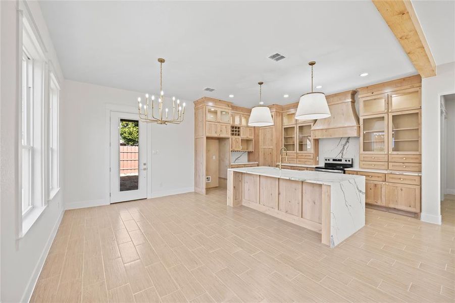 Kitchen with a center island with sink, light wood finish cabinetry, hanging lights, electric range, and wood finish floors Kitchen with a center island with sink, light wood finish cabinetry, hanging lights, electric range, and wood finish floors