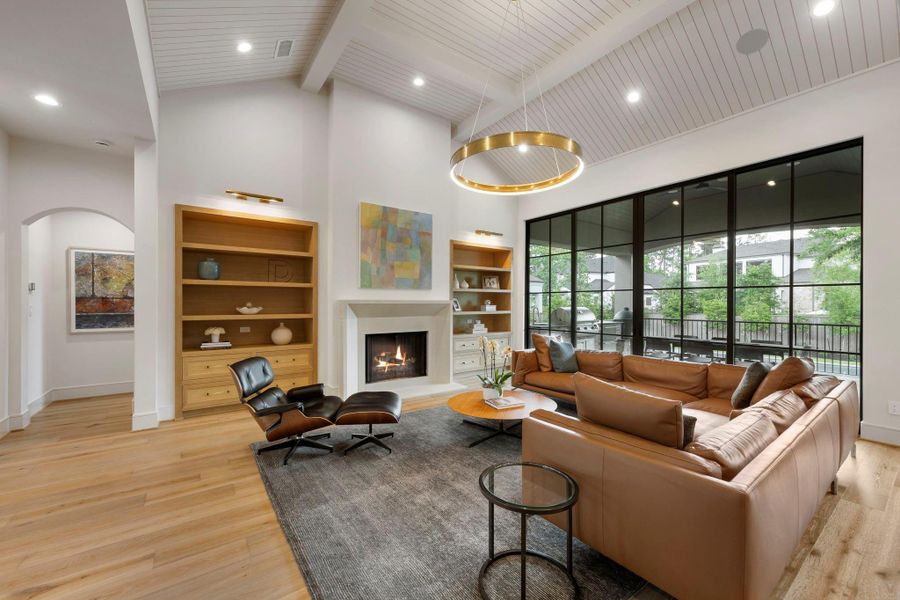 Grand living space featuring soaring architectural ceilings, refined built-in cabinetry, and a statement fireplace, with large sliding doors that extend the space to the covered patio.
