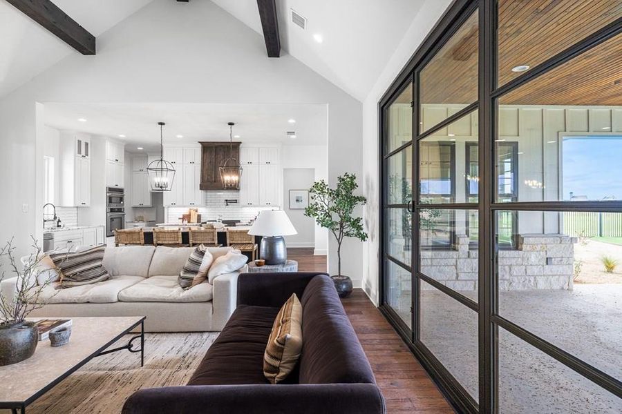 Virtually staged Living area featuring dark engineered wood-style floors, beamed ceiling, recessed lighting, a chandelier, high vaulted ceiling and folding-wall door to covered patio Virtually staged Living area featuring dark engineered wood-style floors, beamed ceiling, recessed lighting, a chandelier, high vaulted ceiling and folding-wall door to covered patio