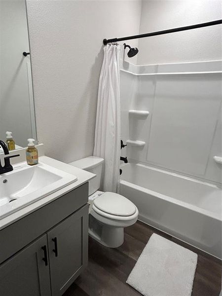 Full bath with vanity, shower / tub combo with curtain, dark wood-style flooring, and a textured wall Full bath with vanity, shower / tub combo with curtain, dark wood-style flooring, and a textured wall