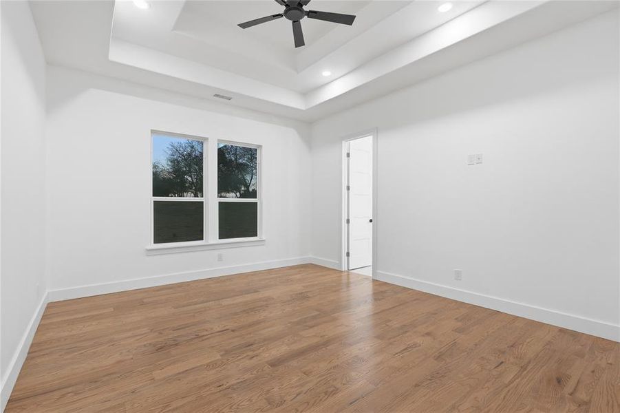 Unfurnished room featuring a ceiling fan, wood finished floors, recessed lighting, and a tray ceiling
