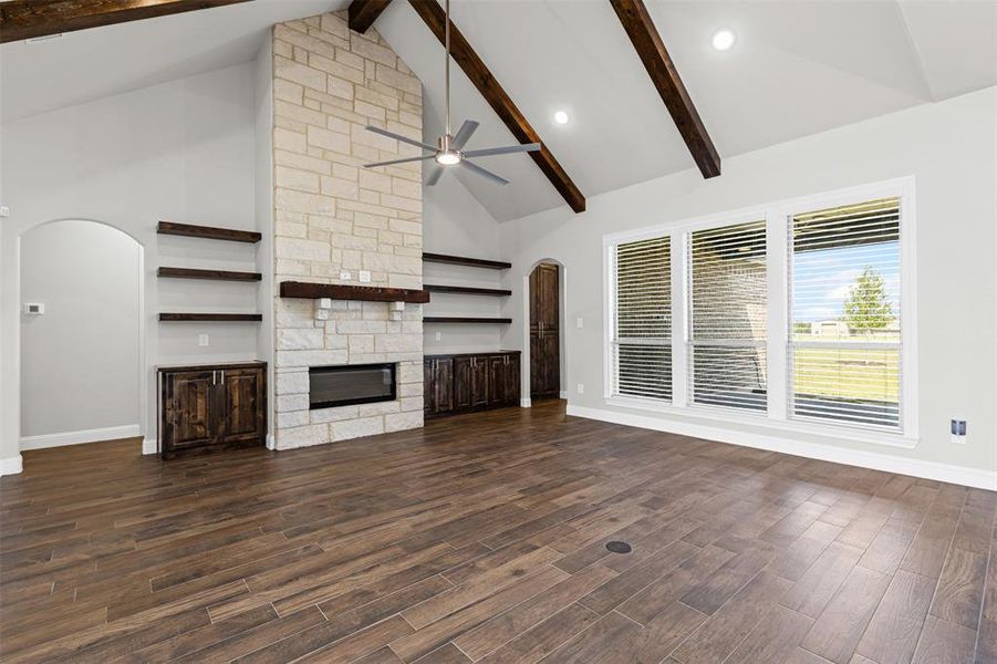 Unfurnished living room with arched walkways, high vaulted ceiling, beamed ceiling, a fireplace, and dark wood-style floors Unfurnished living room with arched walkways, high vaulted ceiling, beamed ceiling, a fireplace, and dark wood-style floors