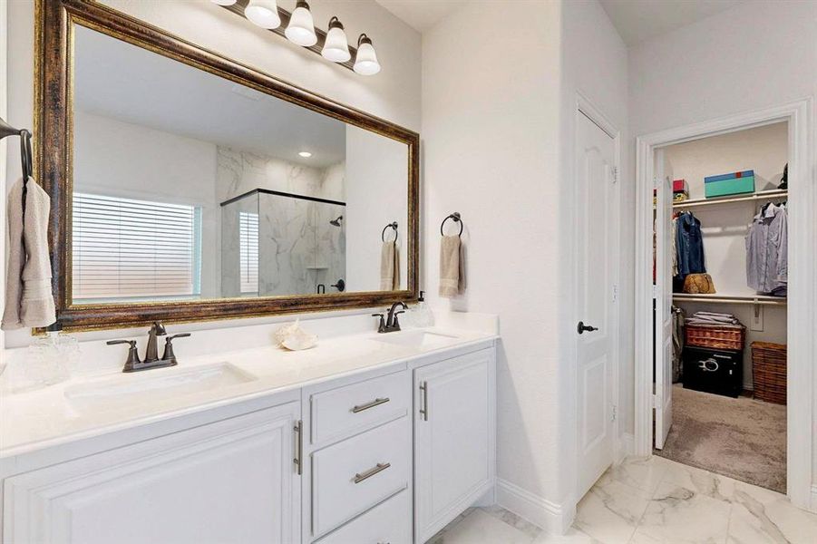Bathroom with light marble finish flooring, a marble finish shower, double vanity, and a walk in closet