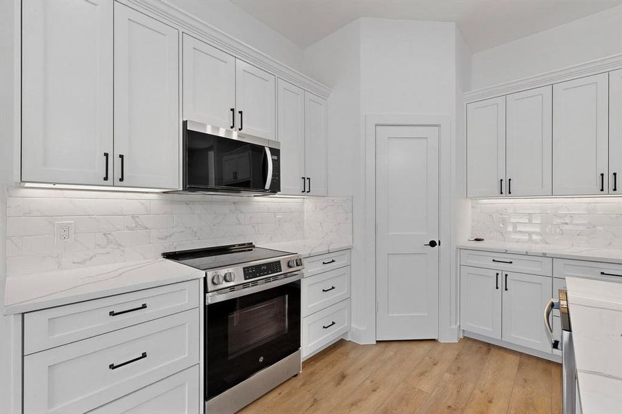 Kitchen featuring appliances with stainless steel finishes, white cabinetry, light stone counters, and light wood-style floors