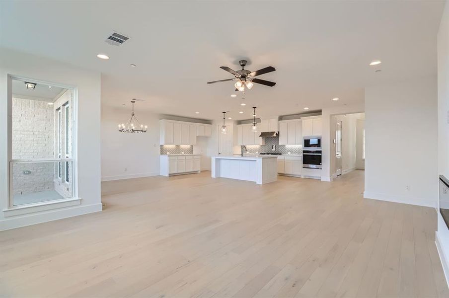 Unfurnished living room featuring ceiling fan with notable chandelier, light hardwood / wood-style flooring, and sink