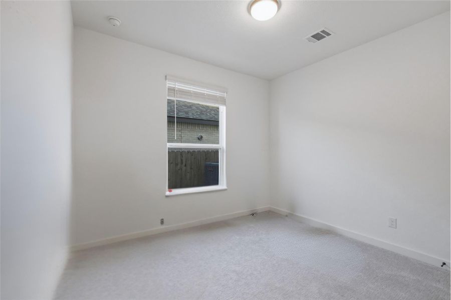 A well-lit room awaits your personal touch, featuring a window and plush carpeting.