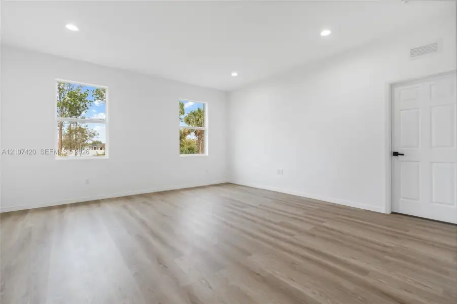 Interior space featuring wood-finish flooring, recessed lighting, dual windows, and a six-panel door with matte black hardware Interior space featuring wood-finish flooring, recessed lighting, dual windows, and a six-panel door with matte black hardware