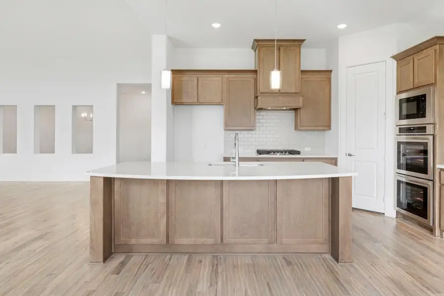 Kitchen with large curved island, wood cabinets, white countertops, subway tile backsplash, and double wall ovens Kitchen with large curved island, wood cabinets, white countertops, subway tile backsplash, and double wall ovens