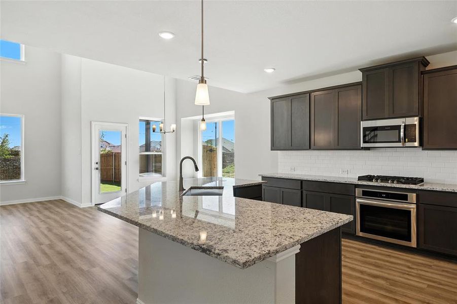 Kitchen with appliances with stainless steel finishes, wood finished floors, an island with sink, tasteful backsplash, and recessed lighting Kitchen with appliances with stainless steel finishes, wood finished floors, an island with sink, tasteful backsplash, and recessed lighting