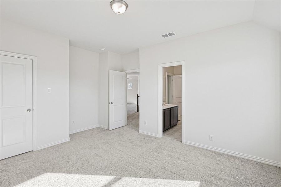 Unfurnished bedroom featuring connected bathroom, light colored carpet, and vaulted ceiling