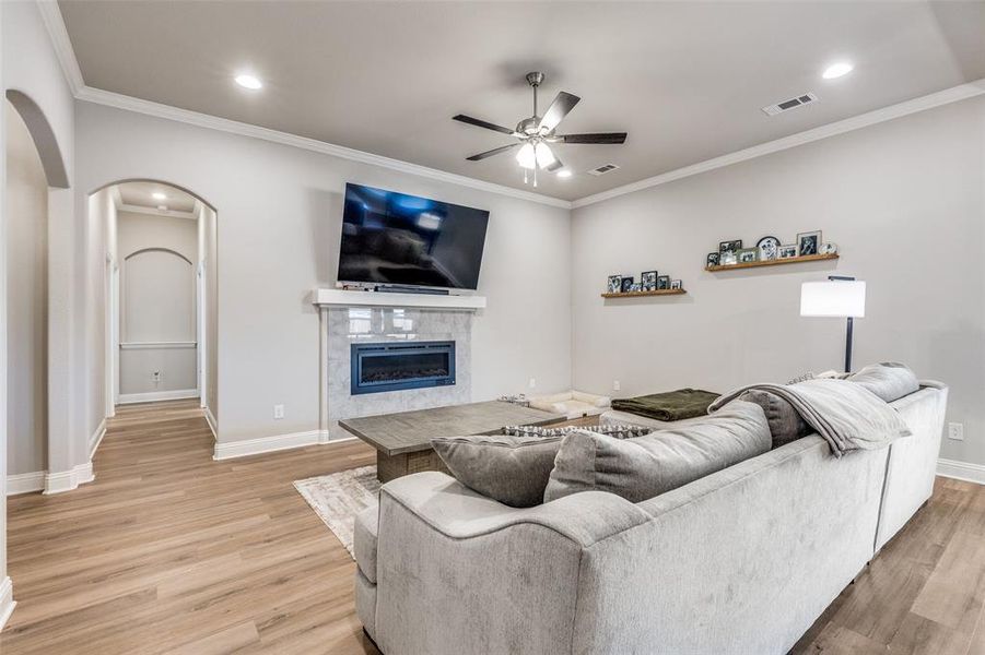 Living area featuring arched walkways, a tiled fireplace, crown molding, light wood-style floors, and recessed lighting Living area featuring arched walkways, a tiled fireplace, crown molding, light wood-style floors, and recessed lighting