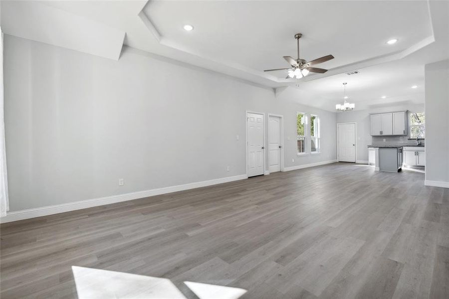 Unfurnished living room with a raised ceiling, ceiling fan with notable chandelier, and light hardwood / wood-style flooring