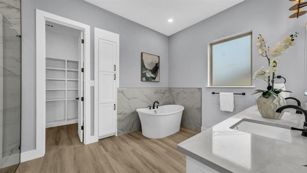 Bathroom featuring tile walls, a freestanding tub, a spacious closet, double vanity, and light wood finished floors