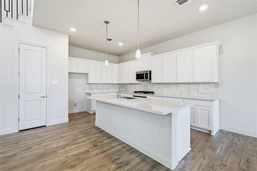 Kitchen with white cabinetry, pendant lighting, a center island with sink, stainless steel appliances, and light wood-style flooring