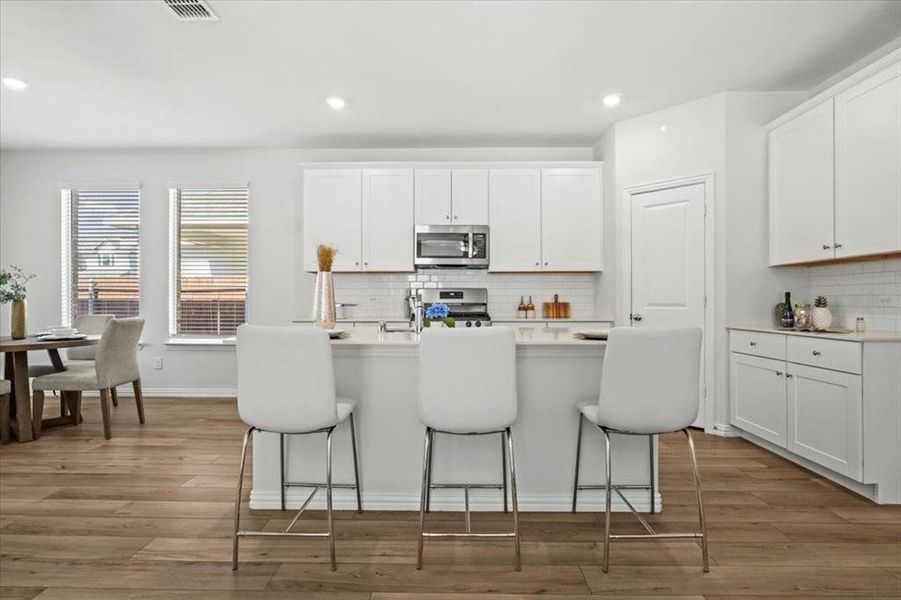 Kitchen featuring white cabinets, tasteful backsplash, a kitchen island with sink, a breakfast bar area, and recessed lighting Kitchen featuring white cabinets, tasteful backsplash, a kitchen island with sink, a breakfast bar area, and recessed lighting