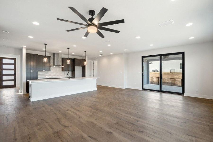 Kitchen featuring open floor plan, a large island, plenty of natural light, wall chimney range hood, and recessed lighting