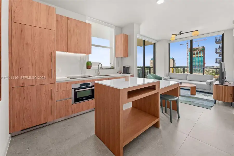 Kitchen featuring wood-finish cabinetry, stone-surface countertops, an integrated island with built-in storage, large-format tile flooring, and floor-to-ceiling windows