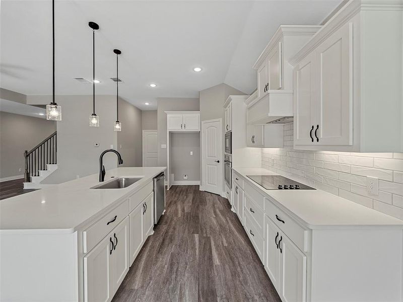 Kitchen featuring decorative light fixtures, white cabinets, dark wood-type flooring, tasteful backsplash, and a kitchen island with sink Kitchen featuring decorative light fixtures, white cabinets, dark wood-type flooring, tasteful backsplash, and a kitchen island with sink