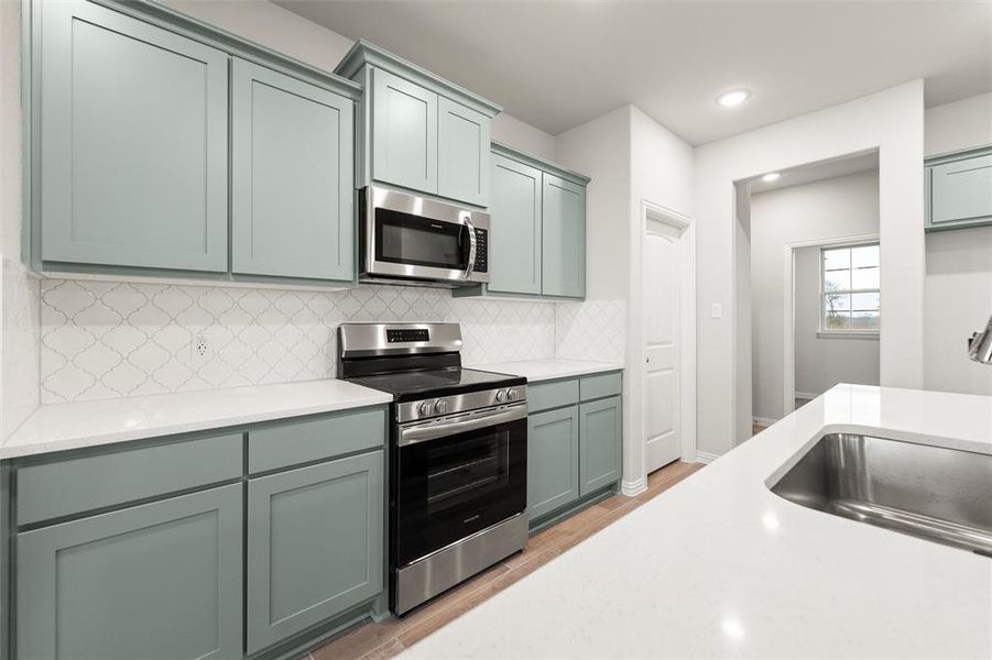 Kitchen with stainless steel appliances, light stone countertops, backsplash, light wood-style flooring, and recessed lighting Kitchen with stainless steel appliances, light stone countertops, backsplash, light wood-style flooring, and recessed lighting