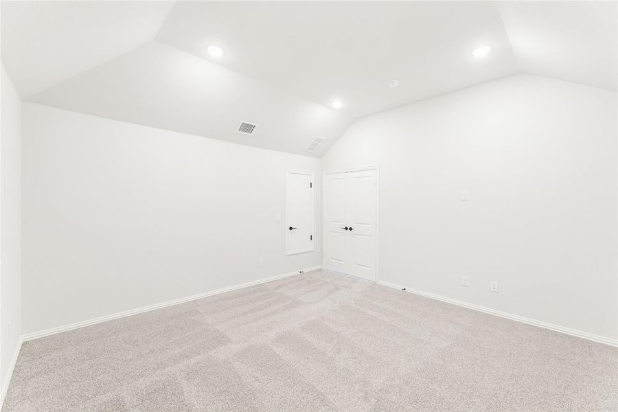 Empty bedroom with vaulted ceiling, recessed lighting, carpet flooring, and two white doors