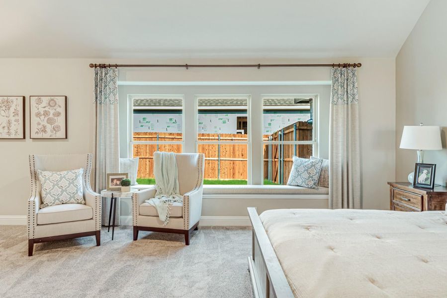 Bedroom with large triple window, window seat, two accent chairs, and neutral carpet
