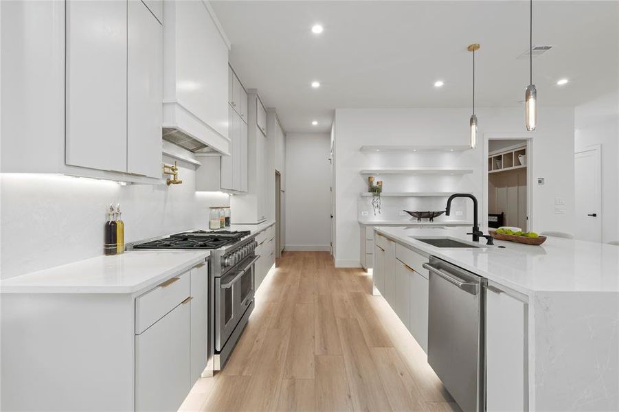 Kitchen with stainless steel appliances, recessed lighting, white cabinets, a center island with sink, and light wood-type flooring