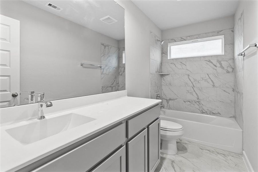 Secondary bath features tile flooring, bath/shower combo with tile surround, stained wood cabinets, beautiful light countertops, mirror, sleek fixtures and modern finishes.