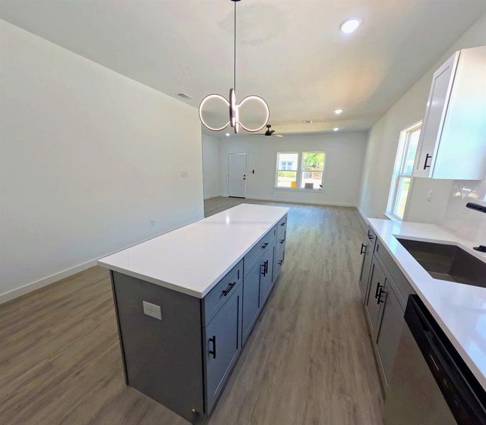 Kitchen with a center island, open floor plan, light wood-type flooring, decorative light fixtures, and stainless steel dishwasher Kitchen with a center island, open floor plan, light wood-type flooring, decorative light fixtures, and stainless steel dishwasher