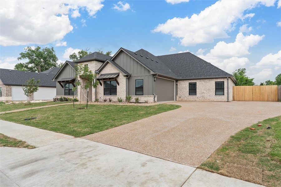 View of front of home featuring a garage, fence, brick siding, board and batten siding, and driveway