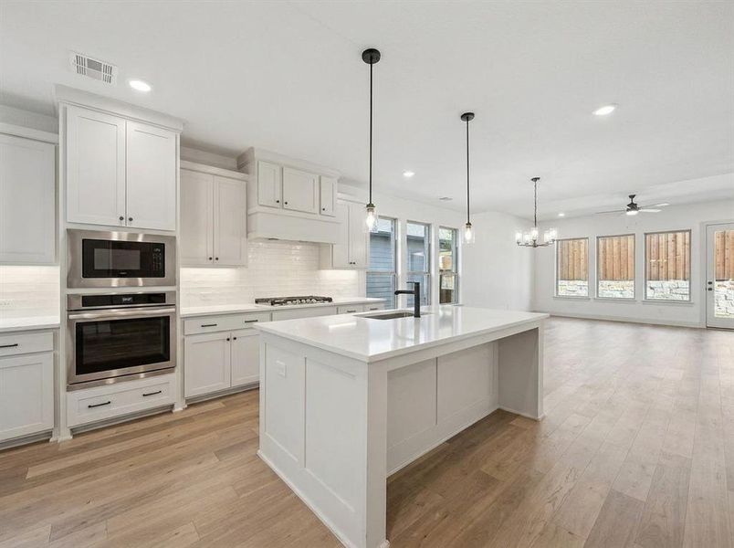 Modern kitchen featuring an island with a sink and pendant lighting, stainless steel appliances, white cabinetry, wood-finish flooring, and a subway tile backsplash