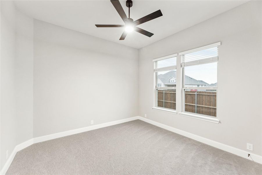 Empty bedroom with gray carpet, ceiling fan, and double windows with backyard view