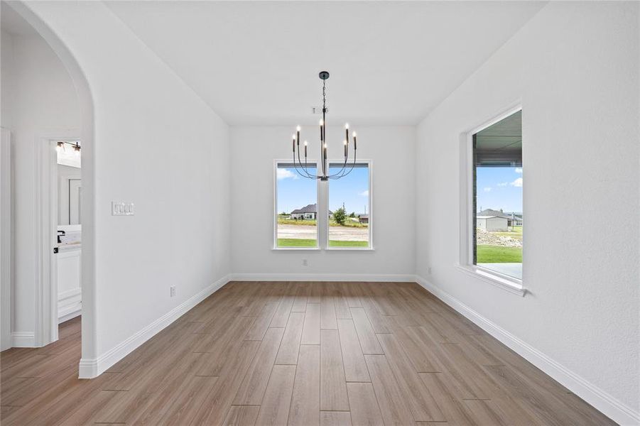 Unfurnished dining area with a chandelier, arched walkways, and light wood-style flooring