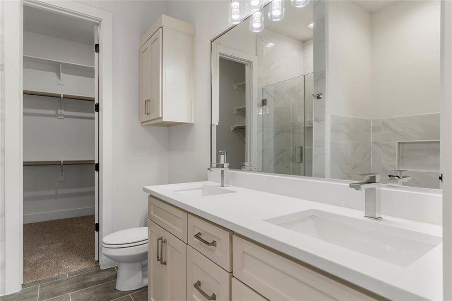 Bathroom featuring a marble finish shower, a spacious closet, and double vanity Bathroom featuring a marble finish shower, a spacious closet, and double vanity