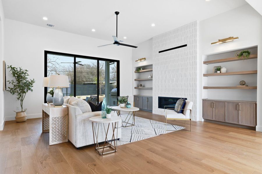 Living room featuring light wood-style floors, a fireplace, ceiling fan, built in shelves, and recessed lighting